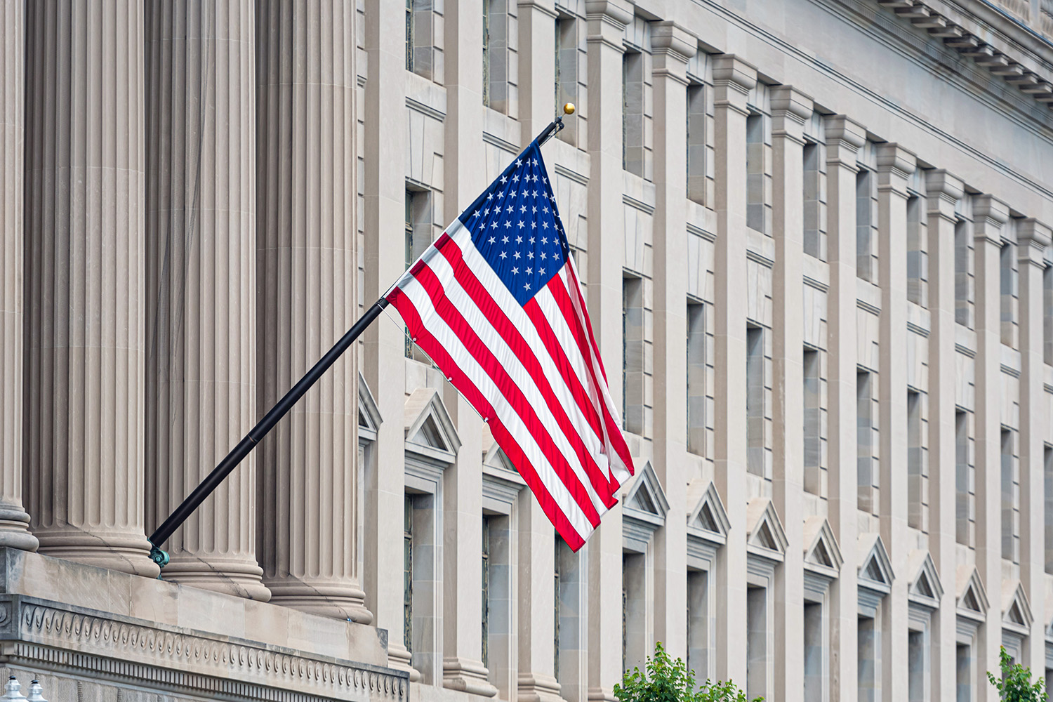 An American flag hangs at an angle on a pole outside a large stone government building with tall columns and rows of windows, enhanced by a modern Building Automation System.