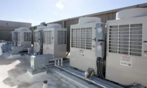 A row of industrial HVAC units installed on a flat rooftop, integrated with a Building Automation System, surrounded by metal pipes and electrical components under a clear sky.