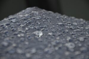 Close-up view of water droplets on a dark surface, possibly fabric or an umbrella, with a blurred background—evoking the precision and environmental control found in a Building Automation System.