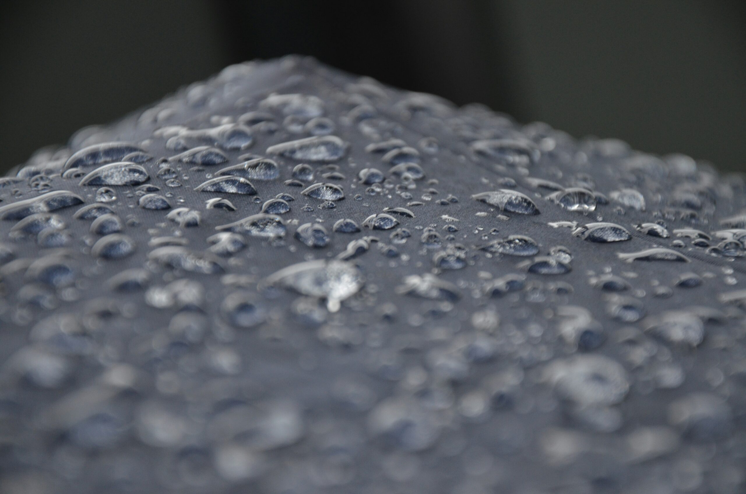 Close-up view of water droplets on a dark surface, possibly fabric or an umbrella, with a blurred background—evoking the precision and environmental control found in a Building Automation System.