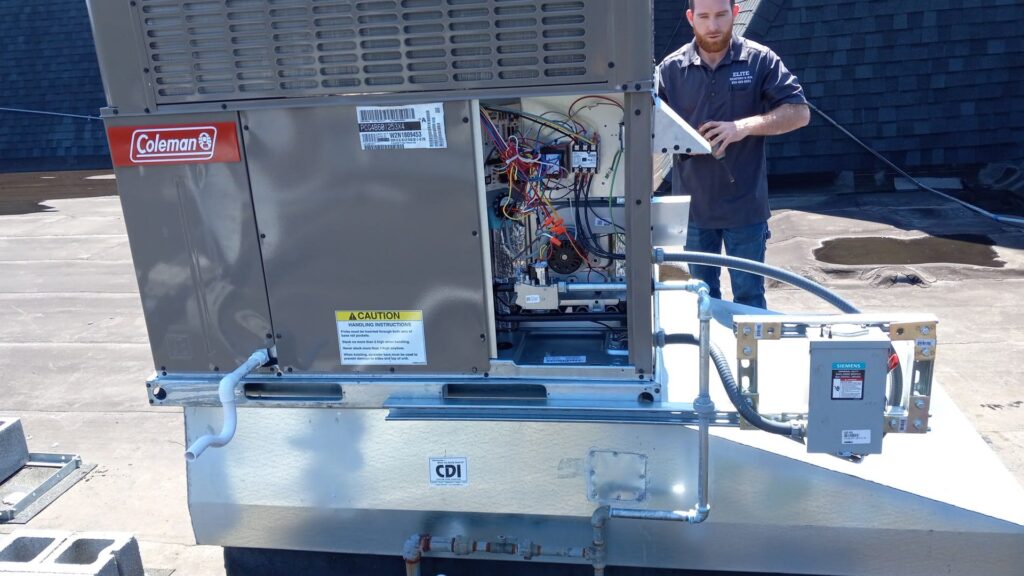 A technician stands next to an open rooftop HVAC unit with exposed wiring and components on a flat roof, working to integrate the system with the building automation system.