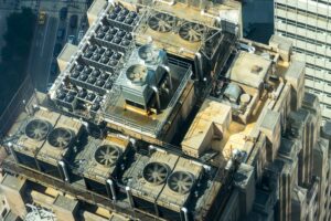 Aerial view of a building rooftop with multiple large industrial HVAC units, fans, ductwork, and machinery arranged in a structured layout, all seamlessly managed by an advanced Building Automation System.