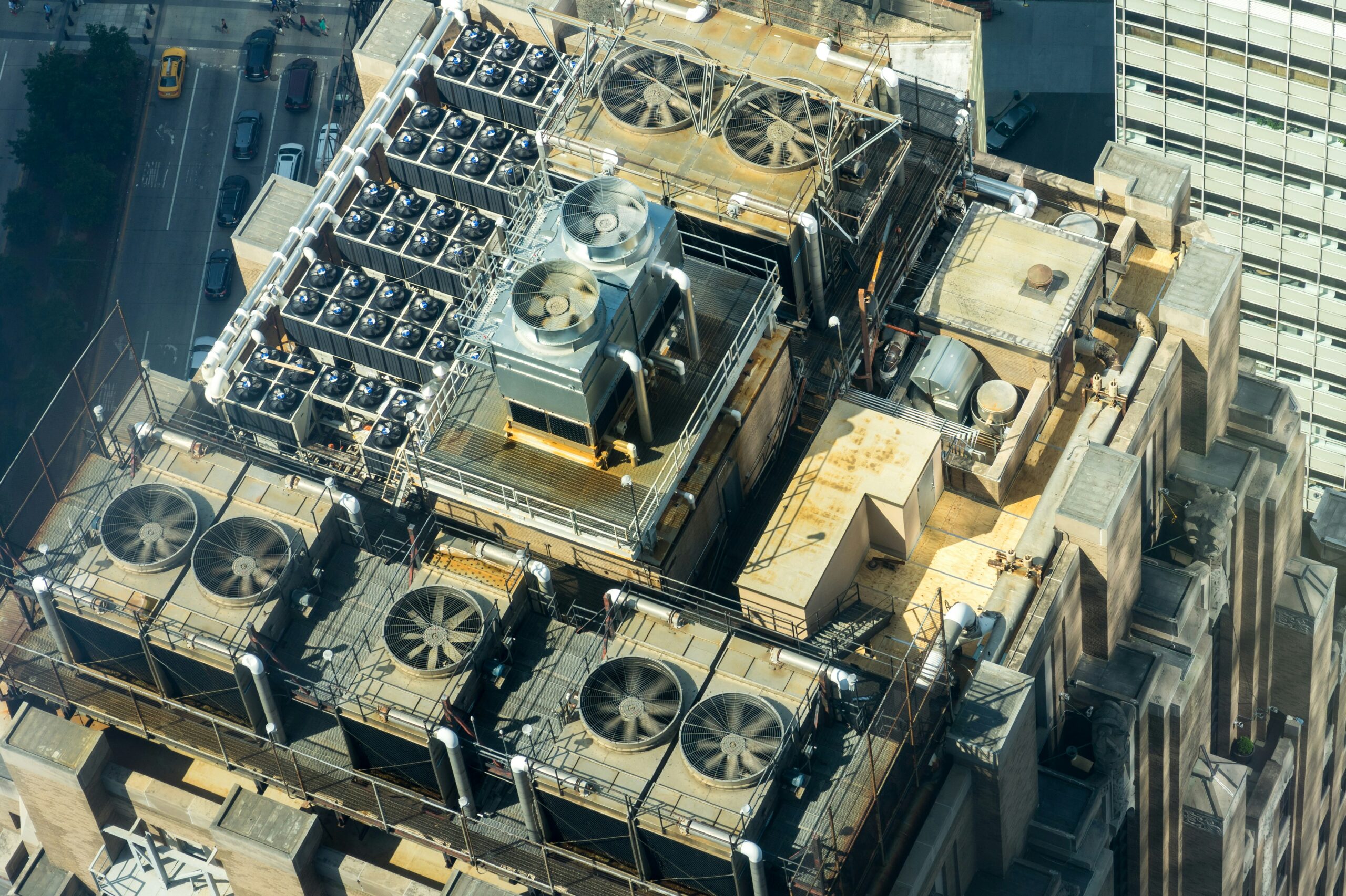 Aerial view of a building rooftop with multiple large industrial HVAC units, fans, ductwork, and machinery arranged in a structured layout, all seamlessly managed by an advanced Building Automation System.