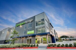 Modern Extra Space Storage facility with a Building Automation System, green signage, large windows, and an office entrance, set against a blue evening sky with a mostly empty parking lot.