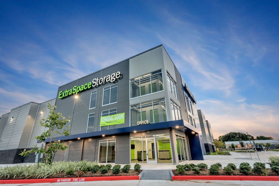 Modern Extra Space Storage facility with a Building Automation System, green signage, large windows, and an office entrance, set against a blue evening sky with a mostly empty parking lot.