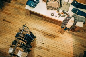 Clothing store interior managed by a Building Automation System, with folded clothes on a table, shirts hanging on a rack, and accessories displayed on a wooden floor.