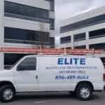A white van with Elite Heating and Air Conditioning Inc. of Cherry Hill and the phone number 856-489-8664 in blue, boasting a red ladder on top, is parked in a lot. Against modern office buildings and leafless trees, it's poised for commercial AC upgrades or fixes.