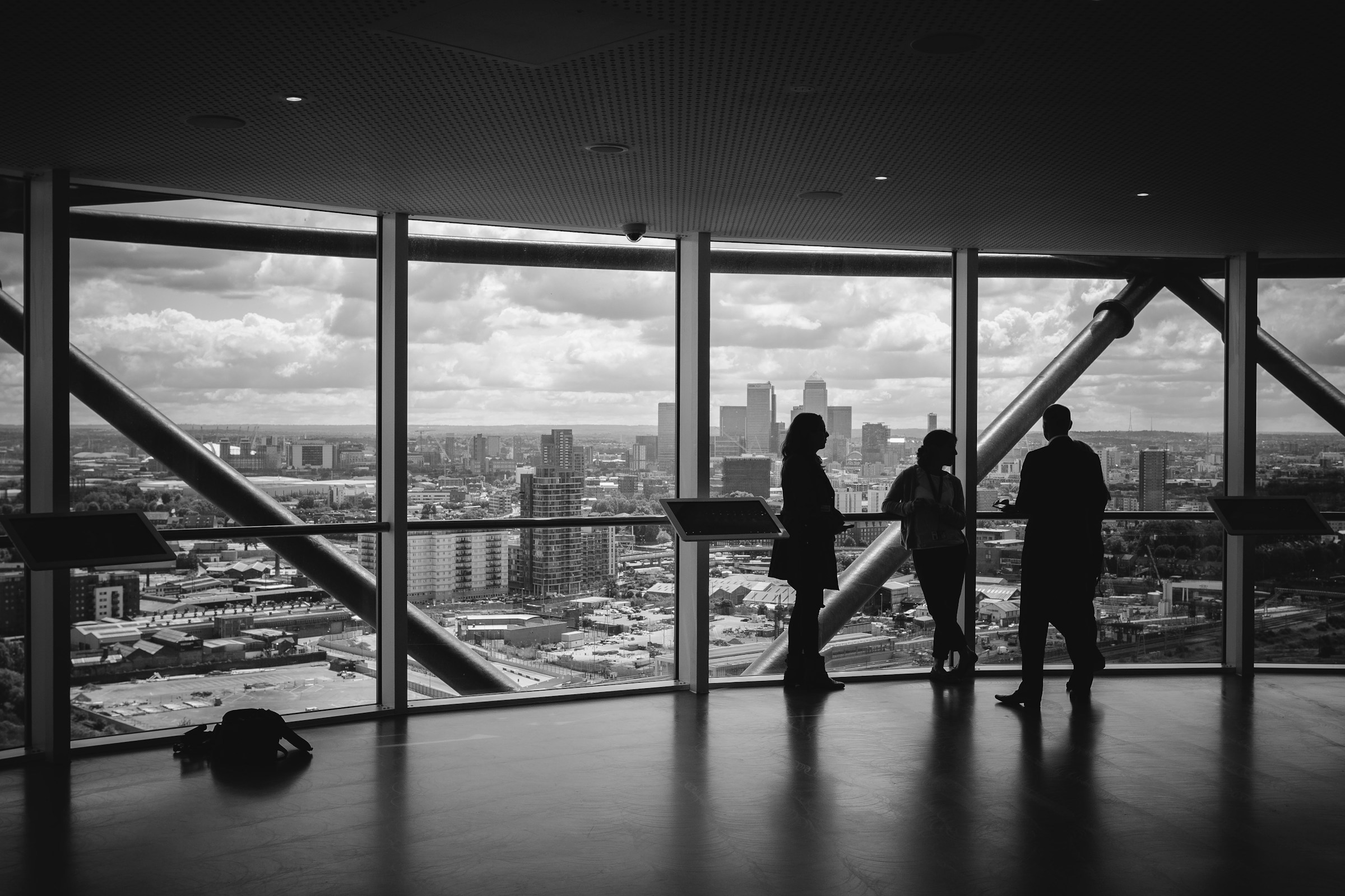 Four people stand and talk inside a high-rise commercial building, overlooking a cityscape through large windows on an overcast day, unaware of the hidden toll that humidity can take on such structures.