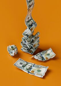 Several U.S. hundred dollar bills are rolled, folded, and stacked against an orange background, with one bill laid flat and another crumpled into a ball—hinting at the hidden toll humidity can take on cash in commercial buildings.