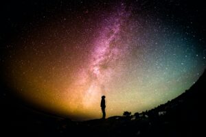A person stands on a hill at night, silhouetted against a colorful, star-filled sky and the Milky Way galaxy—capturing one of those unusual moments that make 2025 unforgettable.