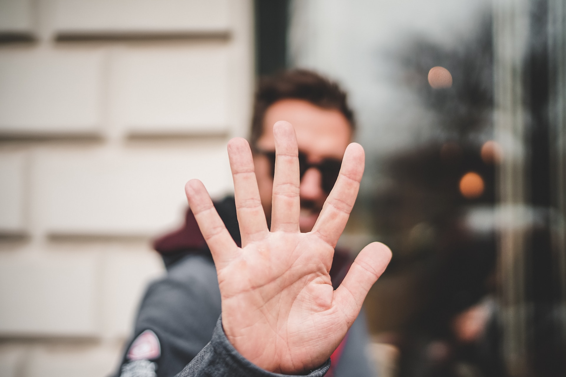 A person stands outdoors with an open hand held up toward the camera, obscuring their face and creating one of those unusual moments. The background is slightly blurred.