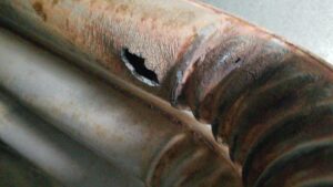 Close-up of a rusted metal pipe with a hole and visible corrosion—an example of Unusual HVAC Moments found during 2025 commercial HVAC inspections.