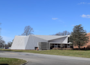 Modern building with angular metal roof and brick walls, set on a grassy lot next to a road under a clear blue sky—an ideal setting for showcasing unusual Commercial HVAC solutions and innovative HVAC Moments 2025.