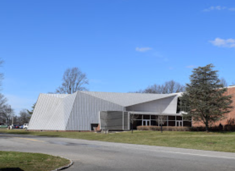 Modern building with angular metal roof and brick walls, set on a grassy lot next to a road under a clear blue sky—an ideal setting for showcasing unusual Commercial HVAC solutions and innovative HVAC Moments 2025.