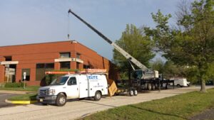 A crane lifts materials near a red brick building, where Elite trucks are parked for a 2025 Commercial HVAC project, capturing one of those unusual moments on a sunny day.