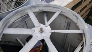 Large metal fan with multiple blades spins inside an industrial cooling tower; a person is partially visible below, performing maintenance work—one of the more Unusual HVAC Moments in commercial HVAC settings for 2025.