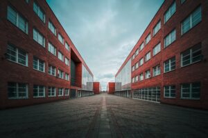 Symmetrical view of two modern red-brick buildings separated by a wide, empty walkway under a cloudy sky—an unusual moment of stillness in this commercial HVAC district, captured ahead of 2025.