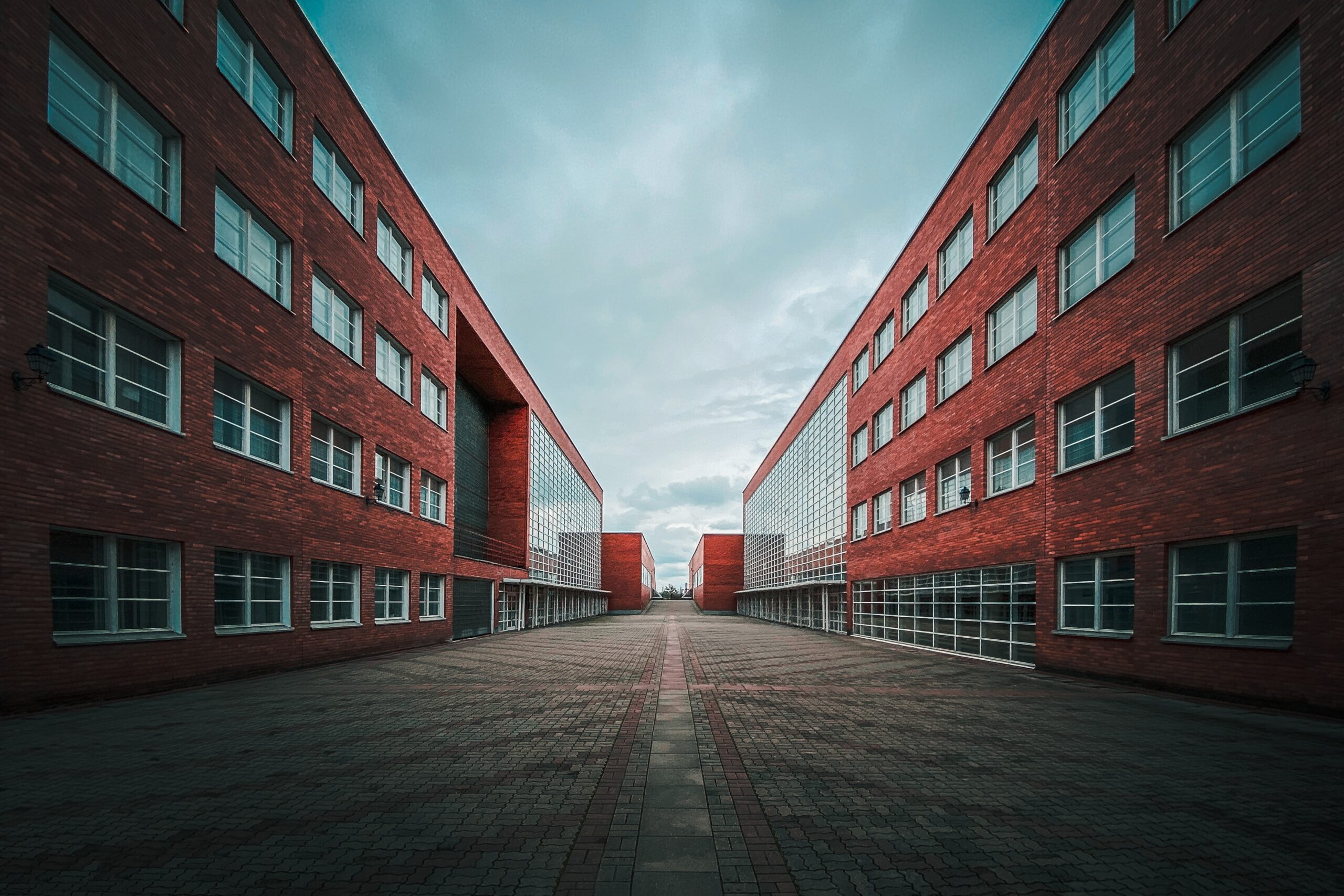 Symmetrical view of two modern red-brick buildings separated by a wide, empty walkway under a cloudy sky—an unusual moment of stillness in this commercial HVAC district, captured ahead of 2025.
