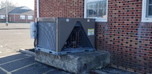 A large Commercial HVAC unit is installed on a concrete platform outside a brick building, near a window and an empty parking lot, ready to deliver reliable climate control for 2025.