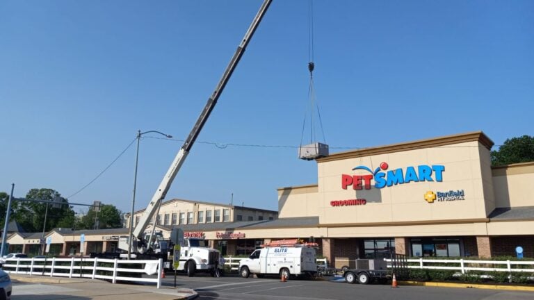 A crane lifts equipment onto the roof of a PetSmart store during an Unusual HVAC Moments commercial project in 2025, while trucks are parked nearby on a clear day.