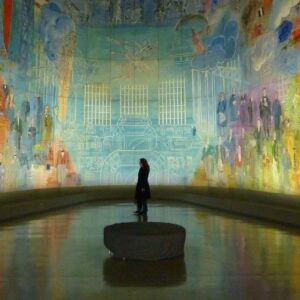 A person stands alone in a circular room surrounded by large, colorful murals depicting various figures and Unusual Moments.