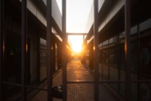 A gated alleyway between modern buildings, with sunlight shining through at the end of the path.