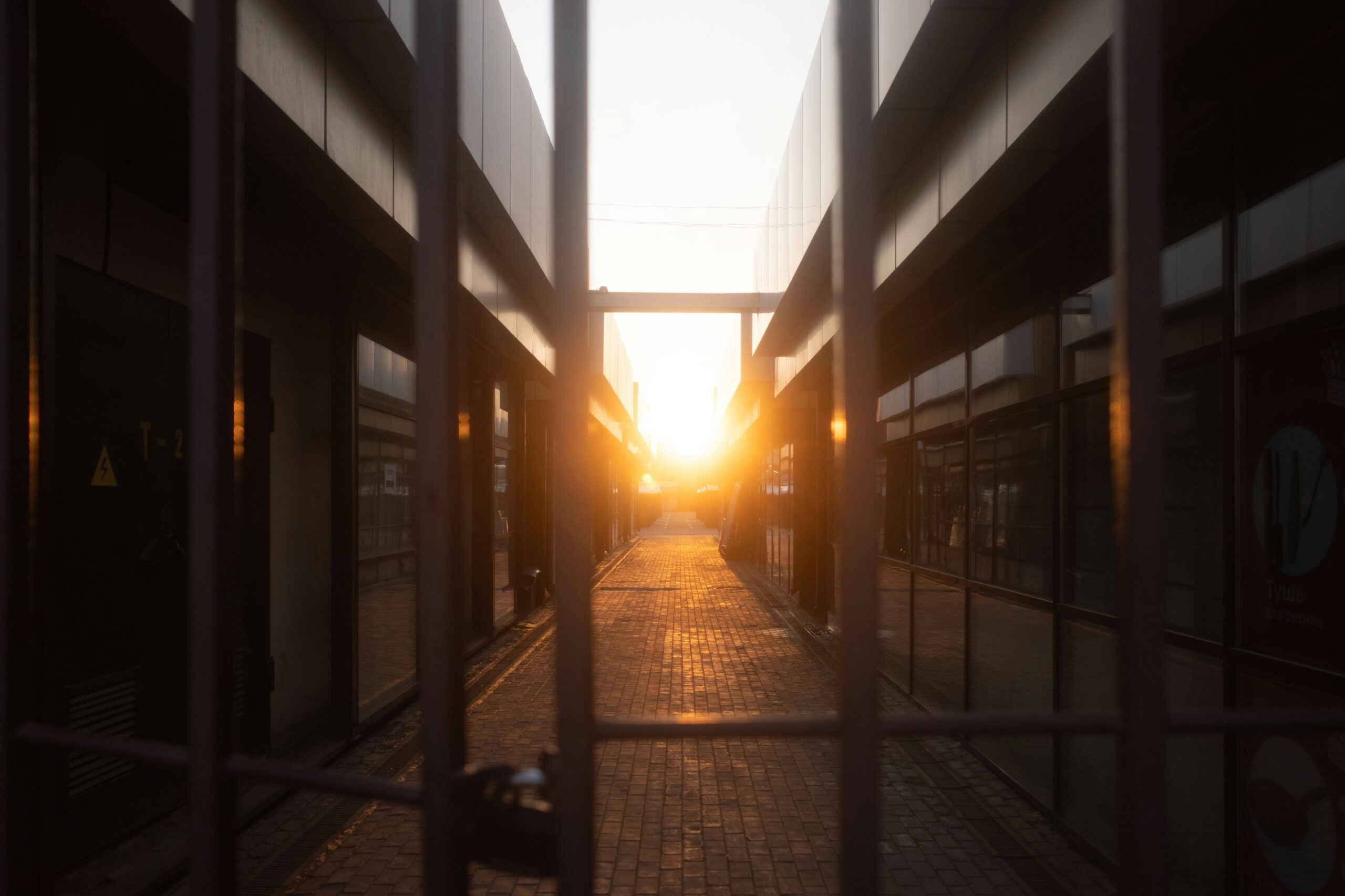 A gated alleyway between modern buildings, with sunlight shining through at the end of the path.