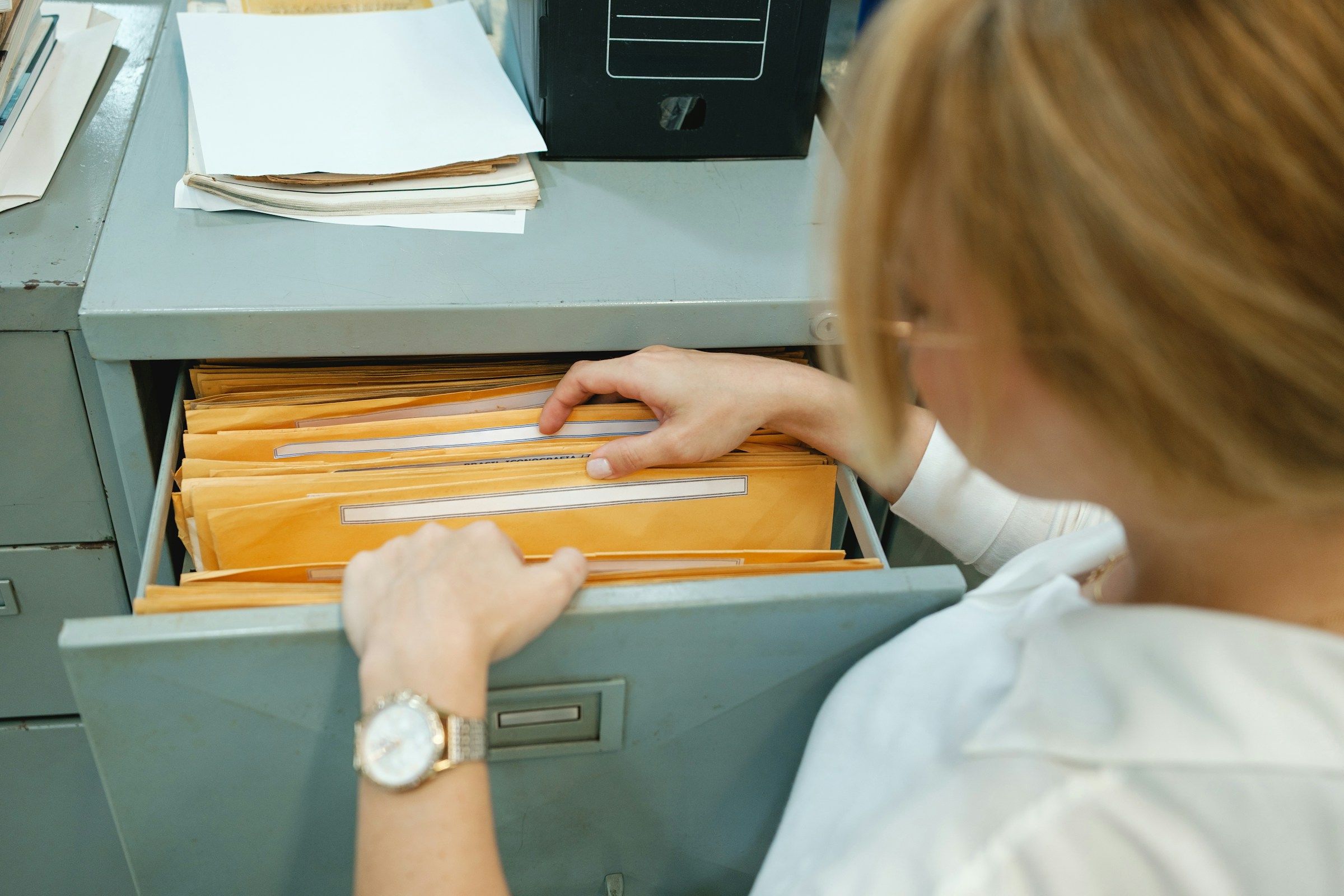 A person in a white shirt is searching through a filing cabinet drawer filled with yellow envelopes and HVAC paper trail documents.